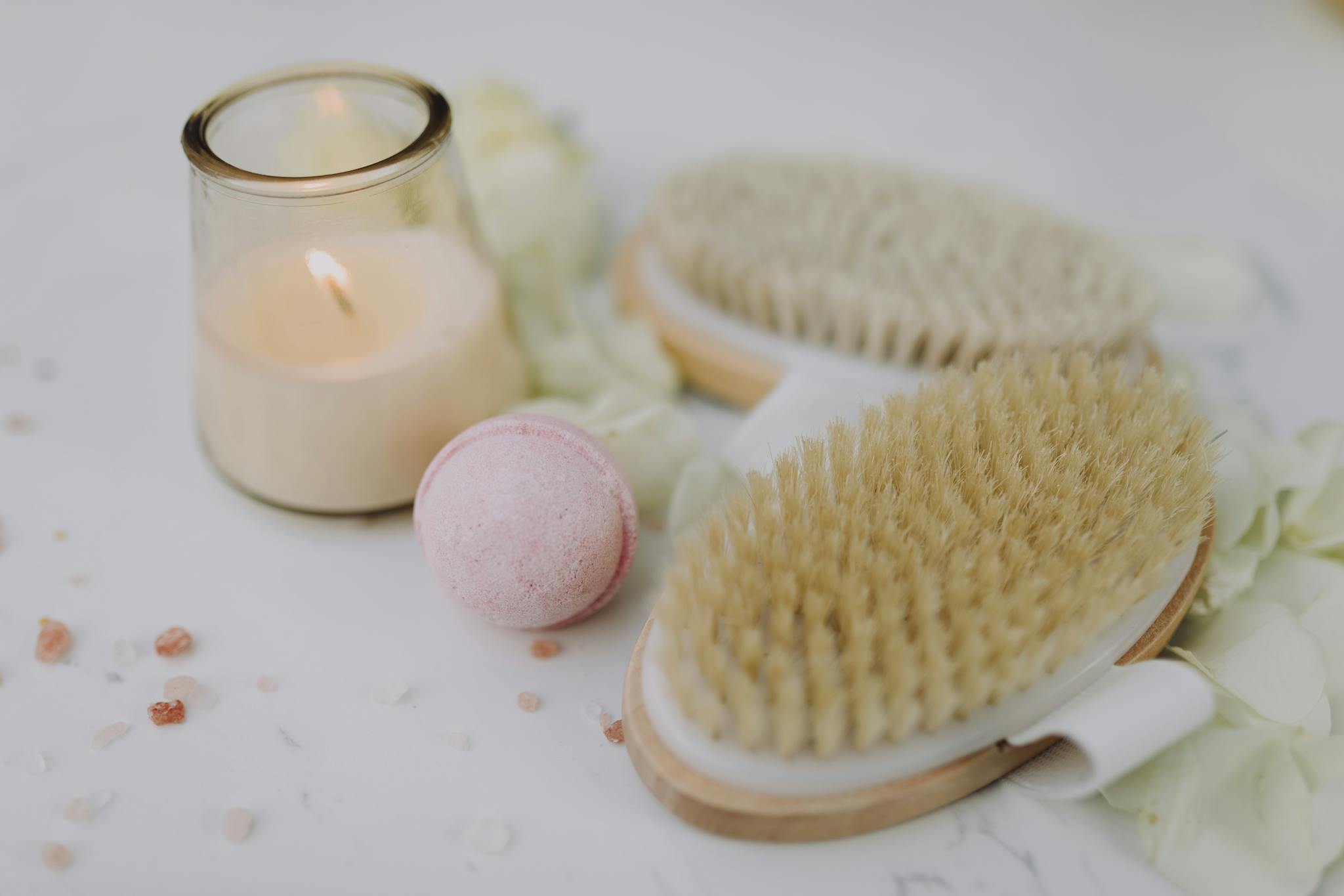 Flat lay of spa essentials including a lit candle, bath brush, and bath bomb for relaxation.